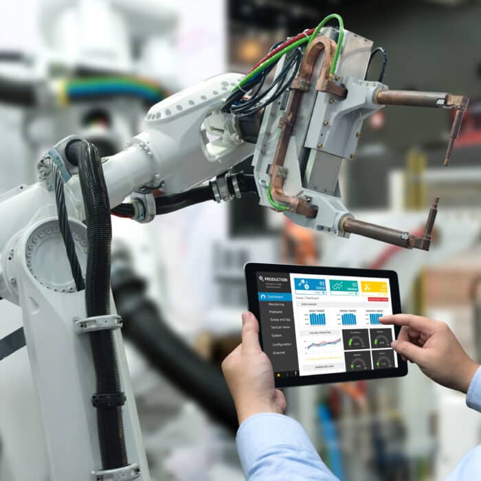 A man oversees an IoT-connected ecosystem controlling a product line, where robots execute tasks autonomously.